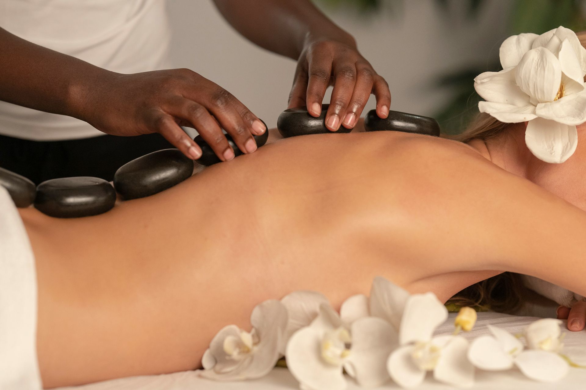 A person receiving a hot stone massage with white flowers on a table